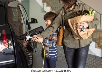 Mother And Son Charging Electric Car At Home. 