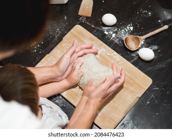 Mother And Son Are Cooking Together. Mom And Toddler Knead Dough From Flour And Eggs On Black Wooden Table. Family Time. Fun At Kitchen. Developing Fine Motor Skills.