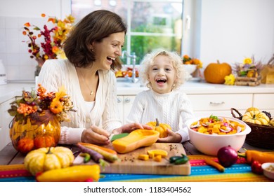 Mother and son cutting pumpkin, onion and carrot, cooking soup for autumn meal. Mom and child cook healthy fall vegetables for family Halloween season lunch. Kids cut squash in kitchen.
