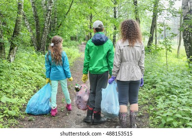 Mother Son And Daughter Clean Up In Urban Woodland, Holding Bags Of Garbage, Seen From Behind