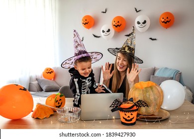 Mother and son dressed in halloween costume sits in a decorated room and communicates on a laptop. Child celebrates Halloween in quarantine in self-isolation, safely remotely with friends.