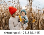 Mother and son exploring corn harvest in background of an agricultural field area. Family playing in the corn maze. Concept of Earth Day, organic gardening, ecology, sustainable lifestyle.