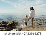 mother and son go into the sea. mother and son test the water with bare feet. mother and son having fun on the seashore. Mum and toddler family time