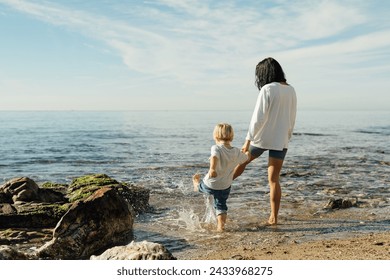 mother and son go into the sea. mother and son test the water with bare feet. mother and son having fun on the seashore. Mum and toddler family time - Powered by Shutterstock