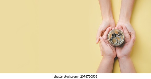 Mother and son hand holding money in glass jar on yellow background, donation, saving, charity, family finance plan concept, fundrasing community care, superannuation, financial crisis concept