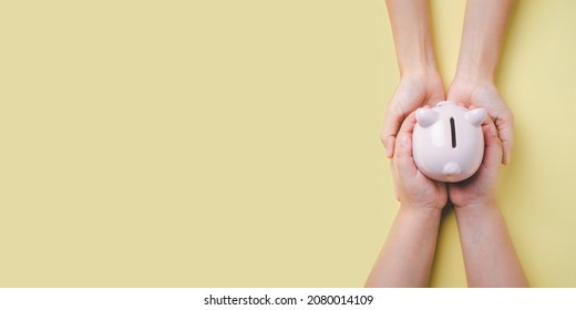 Mother and son hand holding piggy bank on yellow background, saving, charity, family finance plan concept, fundrasing community care, superannuation, financial crisis concept	