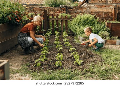 Mother and son hoeing the earth together in the garden.