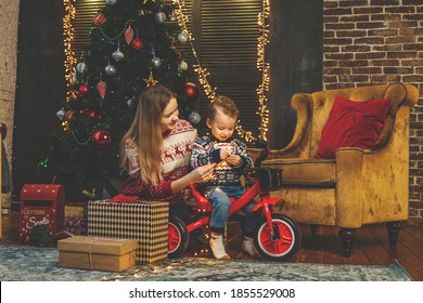 Mother and son hold garland and smile in cozy room. Christmas and new year decoration around. Christmas tree and gift boxes on background. - Powered by Shutterstock