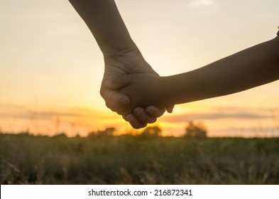 Mother and son holding hands into the sunset of a summer day