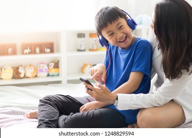 Mother with son listening to music on bed in bedroom - Shutterstock ID 1248829594