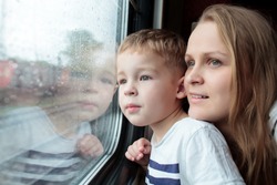 Mutter Und Sohn, Die Durch Ein Zugfenster Schauen, Während Sie Eine Tagesreise Mit Dem Gesicht Der Kleinen Jungen Genießen, Das Sich Im Glas Widerspiegelt