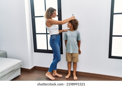 Mother And Son Measuring Child Height Drawing Mark On Wall At Home