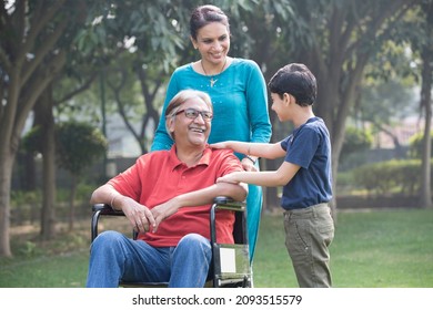 Mother And Son With Old Man In Wheelchair At Park
