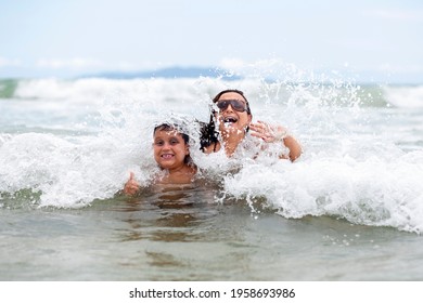 Mother And Son On Vacation Playing In The Sea Wave. Wave Breaking On Your Back And Raising A Splash Of Water. Image For Mother's Day On Vacation.