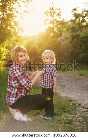 Mother and son in plaid shirts. Woman buttoning buttons on boy shirt. Family time together.