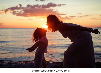 Mother and son playing on the beach at the sunset time. Concept of friendly family. - Powered by Shutterstock