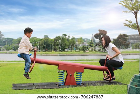 Mother with son playing seesaw in the park.