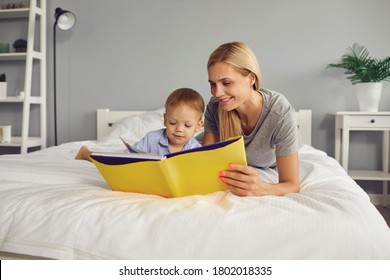 Mother and son are reading a book while lying on the bed in the room. Mothers Day.