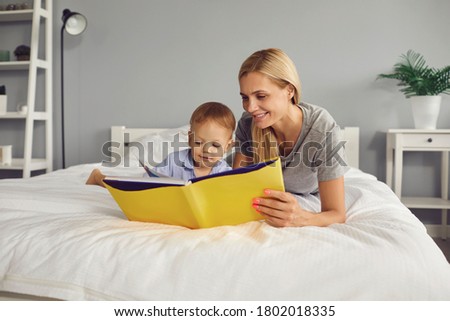 Mother and son are reading a book while lying on the bed in the room. Mothers Day.