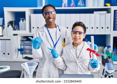 Mother And Son At Scientist Laboratory Pointing Thumb Up To The Side Smiling Happy With Open Mouth 