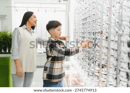Mother and son selecting new frames for vision correction in an optical shop, focusing on eye health and family shopping