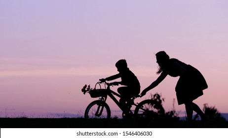 Mother and son silhouette at sunset, parent help child to learn to ride bike, supportive parenting, parent teaching child to develop new skills, shy beginning, develop self confidence