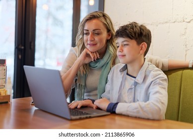 Mother and son sitting in a coffee shop, doing online studying or homework together on a laptop, mom helping her son - Shutterstock ID 2113865906