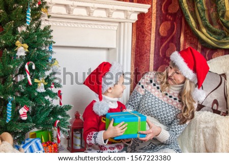 mother and son sitting on the background of a beautiful interior at the Christmas tree. They're holding a gift. Girl and boy smile. They are happy and having a good time. Warm cozy and festive atmosph [[stock_photo]] © 