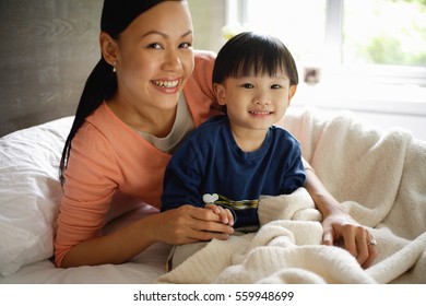 Mother and son in sitting on bed, smiling at camera