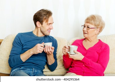Mother and son sitting on couch and drinking tea or coffee