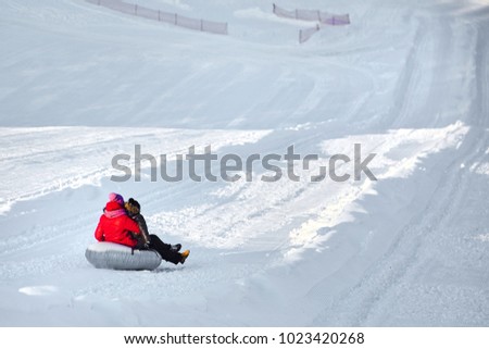 Mother and son sliding  on snow tubing down the hill. Woman and boy having fun sledding on a tube at winter day