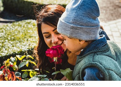 Mother and son smelling the scent of a fucsia rose flower. Mum love concept and parenting representation with a smiling, proud mom close by a red blooming rose allowing her chid to discover the nature - Shutterstock ID 2314036551