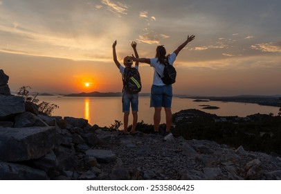 Mother and son standing on rocky mountain trail at sunset, overlooking vast sea and distant islands. Concept of family adventure, outdoor exploration, quality time in nature. High quality photo - Powered by Shutterstock