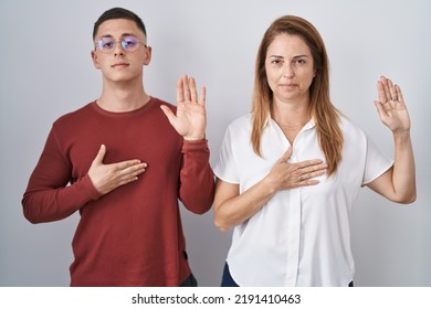 Mother And Son Standing Together Over Isolated Background Swearing With Hand On Chest And Open Palm, Making A Loyalty Promise Oath 