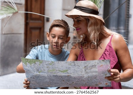 Mother and son studying folded map while navigating unfamiliar European city streets during sunny summer travel day