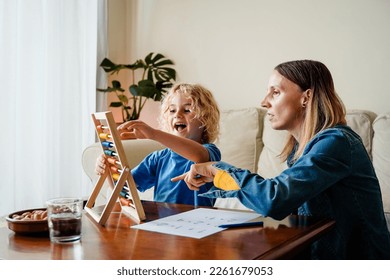 Mother and son studying math with abacus for school class inside home - Family and love concept - Focus on mom face - Powered by Shutterstock