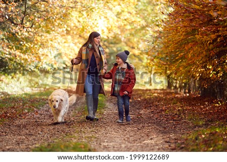Mother And Son Take Pet Golden Retriever Dog For Walk On Track In Autumn Countryside Holding Hands