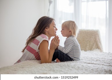 Mother and son, toddler boy, sitting on the bed, holding hands, looking at each other - Powered by Shutterstock