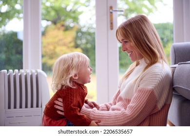 Mother With Son Trying To Keep Warm By Radiator At Home During Cost Of Living Energy Crisis - Shutterstock ID 2206535657