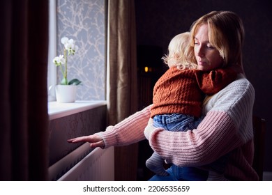Mother With Son Trying To Keep Warm By Radiator At Home During Cost Of Living Energy Crisis - Shutterstock ID 2206535659