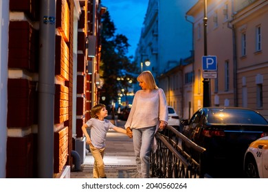 Mother And Son Walking In The City Center Street. Mom And Kid Taking A Summer Evening Walk Outside In The Town. Family Leisure Time. City Life.