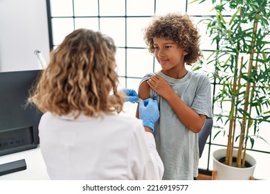 Mother And Son Wearing Doctor Uniform Putting Band Aid On Child Arm At Clinic