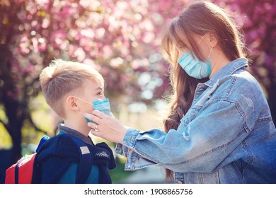 Mother And Son Wearing Face Mask. Family Going To School During Coronavirus Outbreak. Safety Mask For Prevention Covid-19. Woman Puts On Face Mask To Her Child. Stop The Coronavirus Spreading.