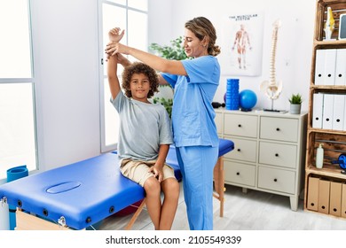 Mother and son wearing physiotherapist uniform having rehab session stretching arm at physiotherapy clinic - Powered by Shutterstock