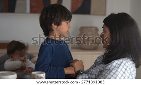 Mother speaking gently to son while holding him on her lap as baby watches, calmly correcting his behavior and offering guidance with patience and warmth at home