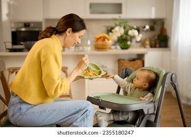 Mother spoon feeding her baby boy in the kitchen - Powered by Shutterstock