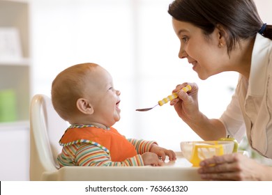 Mother spoon feeding her baby boy. Side view portrait of young woman giving food to kid son
