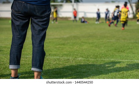 Mother Standing And Watching Her Son Playing Football In A School Tournament On A Clear Sky And Sunny Day. Sport, Active Lifestyle, Happy Family And Soccer Mom Concept.