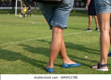 Mother Standing And Watching Her Son Playing Football In A School Tournament On A Clear Sky And Sunny Day. Sport, Active Lifestyle, Happy Family And Soccer Mom Concept.