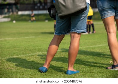 Mother Standing And Watching Her Son Playing Football In A School Tournament On A Clear Sky And Sunny Day. Sport, Active Lifestyle, Happy Family And Soccer Mom Concept.